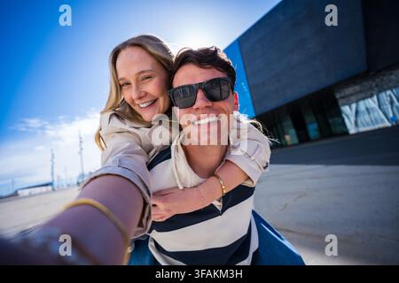 Jeune couple joueur prenant un selfie tout en profitant d'un tour à califourchon sur l'extérieur Banque D'Images