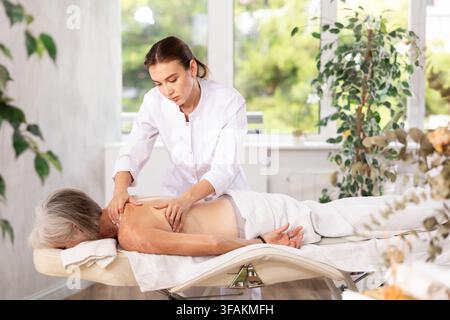 Femme âgée méconnaissable se couche face cachée sur le canapé et profiter de soins spa, massage des épaules Banque D'Images