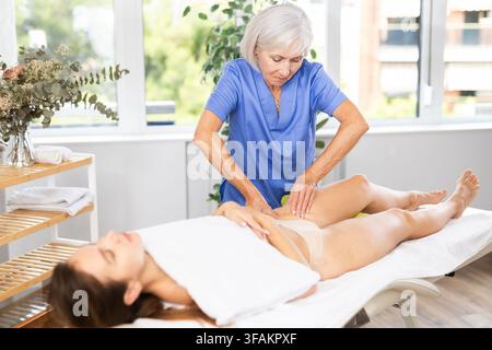 Masseuse professionnelle mature faisant un massage anti-cellulite des cuisses à la jeune femme Banque D'Images