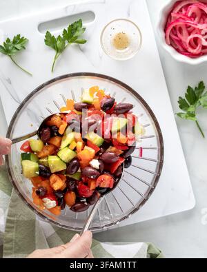 Mains lançant des ingrédients pour préparer une salade méditerranéenne. Banque D'Images