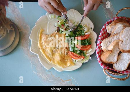 Manger une omelette avec de la salade et du pain sur une table Banque D'Images