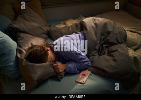 Femme déprimée allongée dans son lit avec un smartphone souffrant d'insomnie Banque D'Images