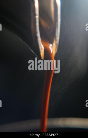 Macro gros plan d'un flux lisse d'un riche espresso versé d'un porte-filtre sans fond dans une tasse. Extraction professionnelle du café. Banque D'Images