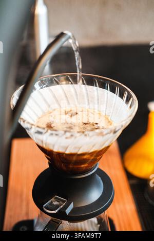 Barista versant de l'eau chaude d'une bouilloire à col de cygne dans un filtre V60 en verre rempli de café moulu. Technique de brassage manuelle. Banque D'Images