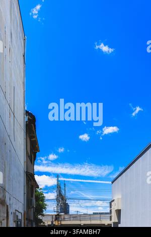 Prise de vue en contre-plongée d'un ciel bleu vif encadré par les façades des bâtiments urbains et les portiques électriques ferroviaires à Osaka, Japon Banque D'Images