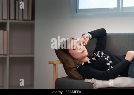 Femme asiatique malade souffrant de maux de tête et de fatigue, allongée sur un canapé à la maison pendant sa maladie Banque D'Images