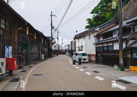 INE, JAPON – 14 JUIN 2026 : Les résidents âgés locaux marchent le long d'une rue tranquille bordée de maisons d'embarcadères Funaya en bois sombre historiques et de magasins traditionnels Banque D'Images