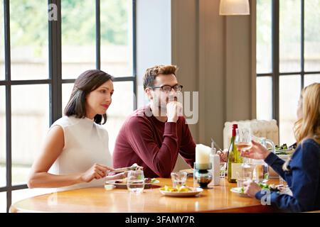 Vin, déjeuner et groupe de personnes à la maison lors d'une réunion, de liens ou de conversation ensemble le week-end. Boisson alcoolisée, nourriture et amis dans la salle à manger pour Banque D'Images