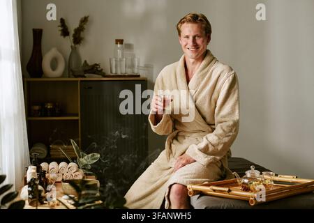 Portrait d'un homme souriant en peignoir buvant du thé à base de plantes dans un salon de spa Banque D'Images