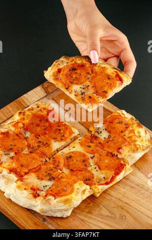 Main de femme prenant une part de pizza au pepperoni Banque D'Images