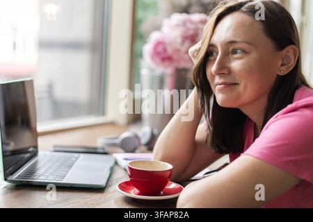 Femme assise à une table de café avec un ordinateur portable et un café Banque D'Images