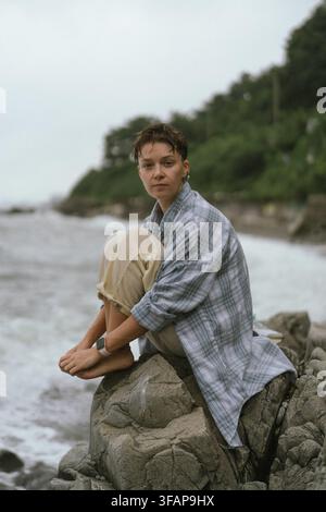 Femme avec une coupe pixie assise sur des rochers au bord de la mer Banque D'Images