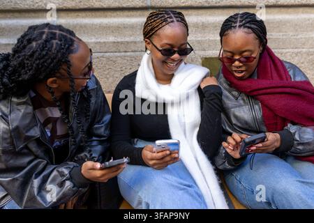 Trois jeunes amis riant ensemble devant leurs smartphones Banque D'Images