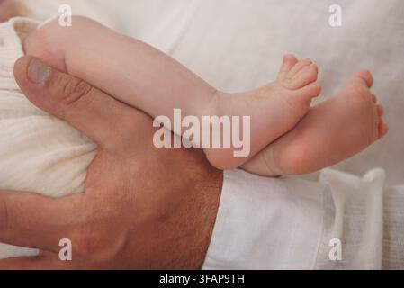 Moment tendre de lien paternel montrant un père berçant un petit pied de bébé contre du linge blanc Banque D'Images