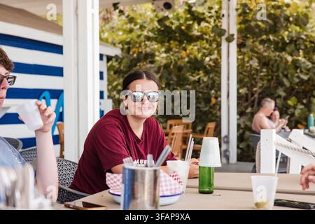 Femme souriante portant des lunettes de soleil dans un café en plein air Banque D'Images