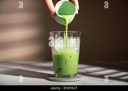 Main versant un latte glacé au thé vert matcha Banque D'Images