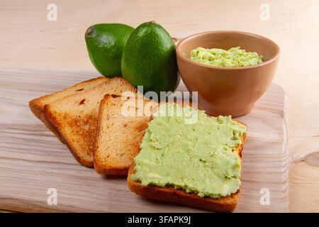 Toast à l'avocat sur pain complet, avocat écrasé sur un plan de travail en bois beige clair. Concept d'alimentation saine Banque D'Images