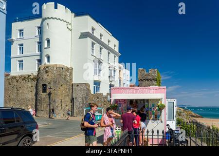 Des gens faisant la queue à un stand rose de café et de glaces à côté des murs de pierre historiques de la ville de Tenby, au Pays de Galles, avec des bâtiments géorgiens blanchis à la chaux au-dessus Banque D'Images