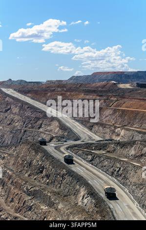 Quatre énormes miennes parcourent une route escarpée sur une grande mine d'or ouverte à Kalgoorlie, en Australie occidentale. Banque D'Images