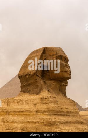 Sphynx devant le fond des Grandes Pyramides égyptiennes. Afrique, plateau de Giza. Une tempête de sable dans l'air donnant un aspect orangé à l'atmosphère. Banque D'Images