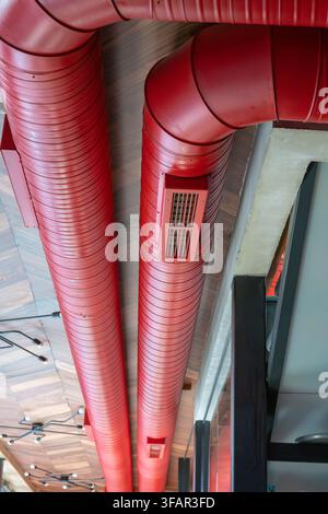 Deux grands conduits de ventilation rouge vif exposés courent parallèlement sur un plafond en bois, mettant en valeur un esthétisme moderne d'intérieur industriel. Banque D'Images
