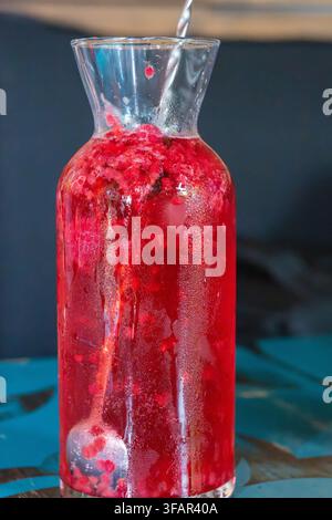 Une boisson glacée rafraîchissante aux baies rouges est servie dans une carafe en verre avec une longue cuillère de bar torsadée et une garniture de feuille fraîche Banque D'Images