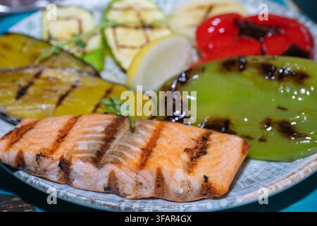 un repas sain mettant en vedette un filet de saumon grillé avec des marques de grill évidentes accompagné de tranches de courgettes, d'aubergines et de poivrons carbonisés, garni Banque D'Images