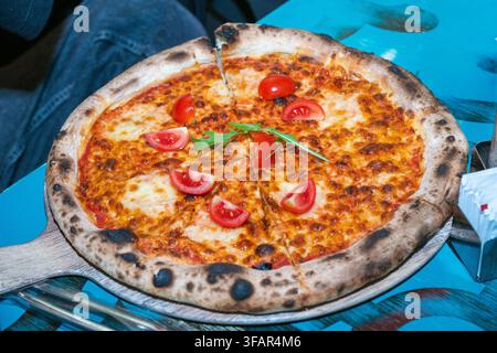 Une pizza Margherita napolitaine fraîchement cuite au feu de bois, garnie de mozzarella fondue, de tomates cerises et d'arugula, servie sur une pelle en bois Banque D'Images