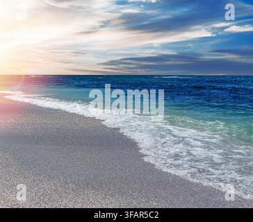 Des vagues douces de la mer déferlent sur une plage de galets pendant un coucher de soleil. Banque D'Images