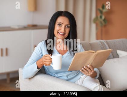 Femme d'âge mûr tenant une tasse de café et un livre Banque D'Images
