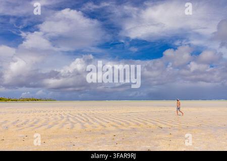 Homme marchant le long de la plage de Honeymoon Island avec un ciel bleu et des nuages sur la lagune d'Aitutaki aux îles Cook Banque D'Images