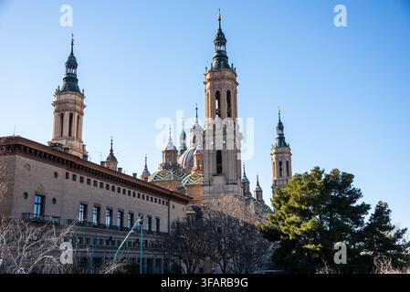 Les hautes tours de la Baslica del Pilar s'élèvent au-dessus des bâtiments et des arbres contre un ciel bleu clair en hiver à Zaragoza, en Espagne Banque D'Images
