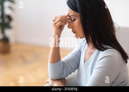 Fatiguée bouleversée femme d'âge moyen massant le pont de nez Banque D'Images