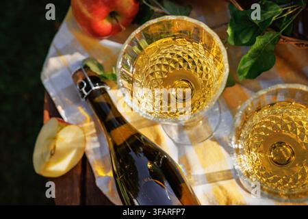 Composition en plongée de cidre doré, bouteille rustique et pommes fraîches sur une table de campagne. Nature morte de récolte lumineuse avec boisson maison Banque D'Images