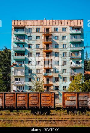 Wagon ferroviaire rouillé à côté d'un immeuble d'appartements de type Brejnevka de l'ère soviétique près de la gare abandonnée de Tchiatura, en Géorgie. Banque D'Images