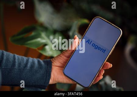 Main tenant un smartphone avec le texte Agent IA visible sur l'écran, entouré de feuilles de plantes vertes floues en arrière-plan Banque D'Images