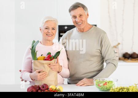 Couple senior tenant un sac d'épicerie dans la cuisine à la maison Banque D'Images