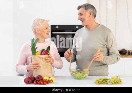 Couple âgé debout avec un forfait plein de provisions dans la cuisine Banque D'Images