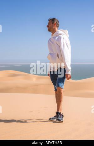 Homme debout sur des dunes de sable surplombant l'océan à Sandwich Harbour en Namibie Banque D'Images