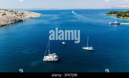 Vue aérienne de voiliers et d'un catamaran naviguant dans les eaux bleues et claires de la mer Adriatique près de la côte rocheuse de Rab, Primorje-Gorski Kotar Banque D'Images