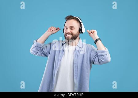 Un jeune garçon heureux dans un casque dansant sur sa chanson préférée, en écoutant de la musique sur fond bleu studio Banque D'Images