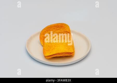 Des chips de tortilla empilées reposent sur une assiette blanche devant un fond uni. Banque D'Images