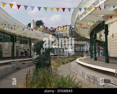 FOLKESTONE, KENT, UK – 24 JUILLET 2026 : Des figures sculpturales se dressent à côté d'un ancien lit ferroviaire planté sous des guirlandes colorées au port de Folkestone. Banque D'Images
