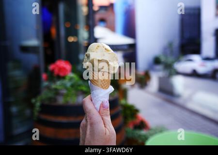 Main tenant une cuillère de glace crémeuse dans un cône en gaufre en plein air par une journée d'été ensoleillée. Banque D'Images
