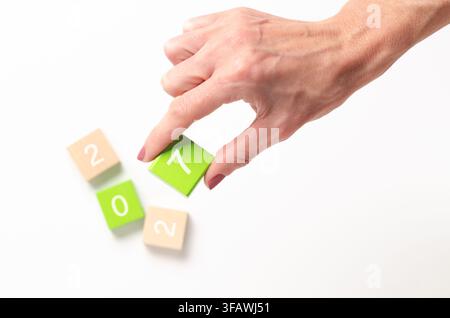 Une main tenant le chiffre sept et des chiffres flous dans des cubes en vert lime et en bois avec les chiffres en blanc, sur fond blanc et espace de copie. Banque D'Images