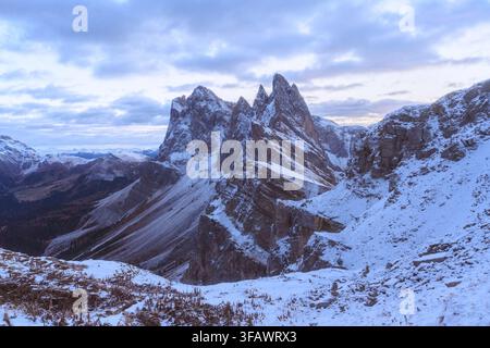Sommets enneigés de la Seceda sous des nuages dramatiques pendant l'heure bleue dans les Dolomites. Paysage alpin accidenté avec neige fraîche et formations de calcaire Banque D'Images