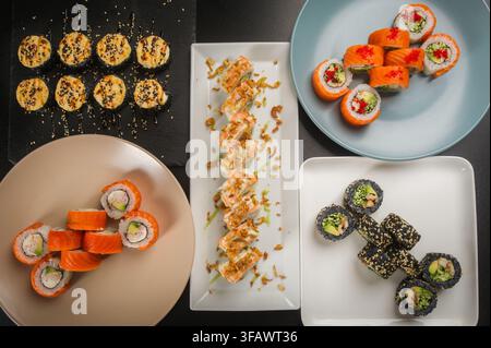 Variété de délicieuses roulades de sushi japonaises présentées sur des assiettes avec différentes garnitures et baguettes en bois, vue de dessus. Banque D'Images