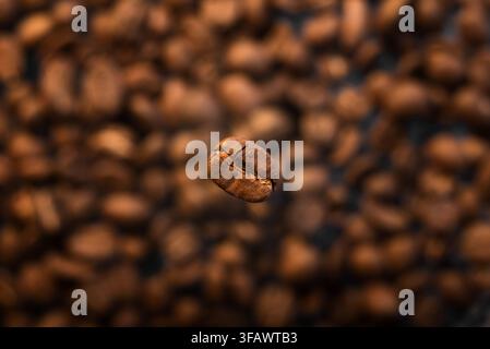 Graine de café torréfiée tombant sur un fond de grains de café noirs Banque D'Images