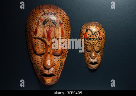 Paire de masques en bois africains ethniques sculptés à la main avec des motifs tribaux complexes et des ornements géométriques accrochés à un mur sombre, gros plan, idéal pour l'intérieur Banque D'Images