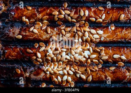Vue macro de dessus montrant la texture détaillée d'un aliment grillé sombre recouvert de graines de sésame dorées et blanches grillées, gros plan Banque D'Images